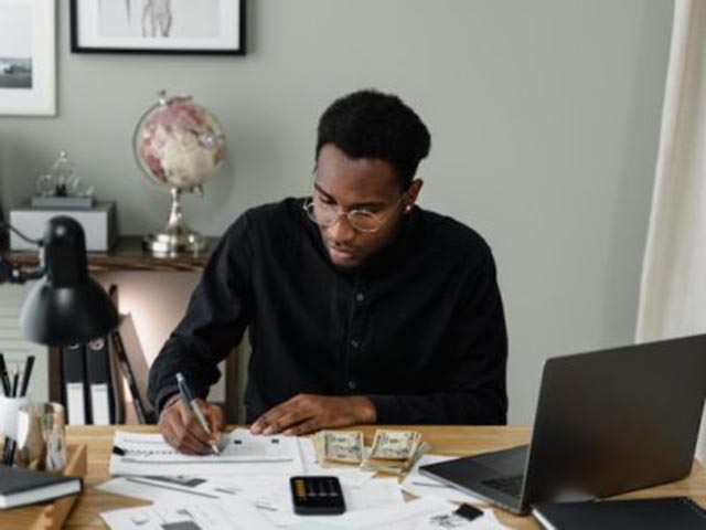 man sitting at a desk reviewing financial documents with a laptop calculator and stacks of cash