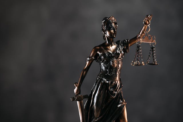 A bronze statue of Lady Justice holding a sword and scales, symbolizing fairness and impartiality in the legal system, set against a dark, blurred background.
